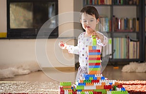 Lovely laughing little child, brunette girl of preschool age playing with colorful blocks sitting on a floor