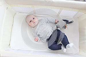 Lovely little 3 months girl with toy lying in travel crib