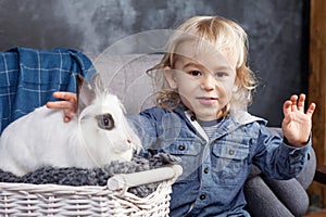 Lovely little boy plays with a white rabbit. The boy smiliing and looking in the camera