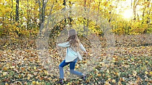 Lovely little girl is dancing alone among fallen maple leaves