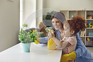 Lovely little girl helping her mother water houseplant at home, copy space text.