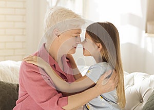 Lovely little girl and her grandma touching noses and embracing at home