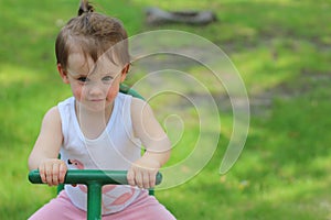 Lovely little girl kindergartner rides on a swing on a playground against a background of green grass photo