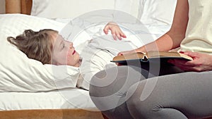 Lovely little girl laughing in her bed, her mother reading her a book before sleep