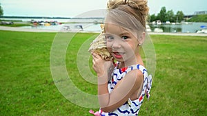 The lovely little girl listens to a big shell to hear noise of waves. Close up