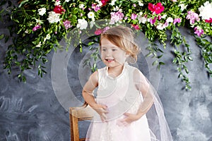 Lovely little girl plays against the flowers background. Portrait of the pretty smiling little girl