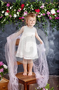 Lovely little girl plays against the flowers background. Portrait of the pretty smiling little girl