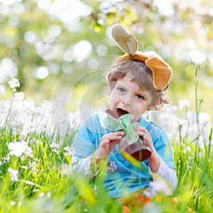 Lovely little kid boy with Easter bunny ears celebrating traditional feast. Happy child eating chocolate rabbit fugure