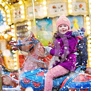 Lovely little kid girl riding on a merry go round carousel horse at Christmas funfair or market, outdoors. Happy child