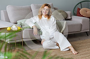 Lovely middle-aged blond woman with a beaming smile sitting on the floor close to the sofa