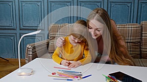 Lovely mother babysitter teacher helping kid daughter with homework, learning drawing at home