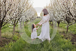 Lovely mother playing with daughter among blooming garden