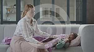 Lovely mother reading book to cute kid on sofa