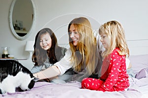 Lovely mother and two little girls daughters cuddling together with cat in bed in morning. Happy family of young single