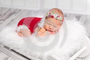 Lovely newborn girl in red romper sleeping on fluffy blanket