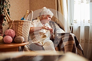 Lovely old woman knitting and using laptop at home