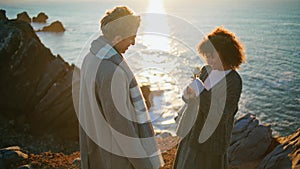 Lovely pair dating sunset sea cliffs closeup. Enamoured man bringing flower