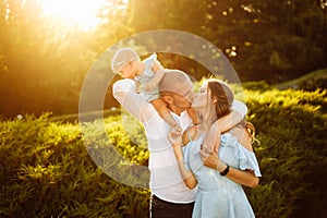 Lovely parents with baby girl, young family walking at the park, smiling, adorable daughter sitting on fathers shoulder