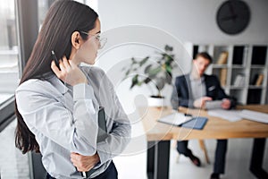 Lovely picture of young confident woman look back at her boss. He sit at table. Guy look at model. She touches her hair