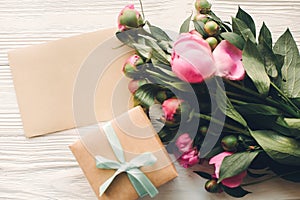 Lovely pink peonies with empty craft card and gift box on rustic white wooden background top view, space for text. floral greeting