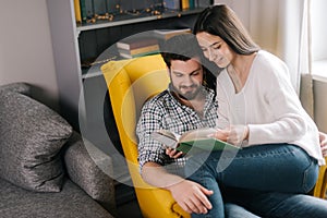 Lovely positive young couple reading a book together, sitting on yellow chair