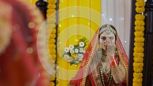 Lovely Punjabi bride putting on Bindi while looking in the mirror - bridal look