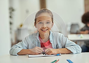 Lovely pupil. Gorgeous little school girl smiling at camera while sitting at the desk in classroom