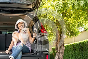 Lovely puppy pomeranian dog with Asia women owner at the back of suv car on travel tip and copy space