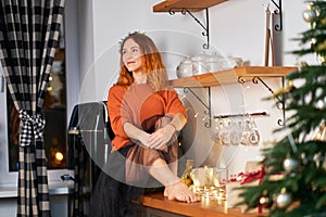 A lovely red-haired girl sits on the roofing cloth in a stylish cozy kitchen decorated for Christmas