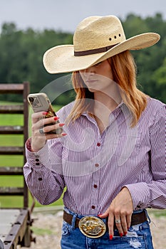 A Lovely Red Headed Cowgirl Uses Her Cellphone In A Country Western Setting Outdoors