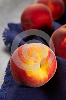 Lovely ripe peaches lie on a blue linen kitchen napkin on the table. Natural fruit. Close up.