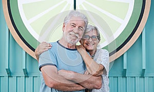 Lovely senior couple hugging and looking at camera standing in city street at sunset light