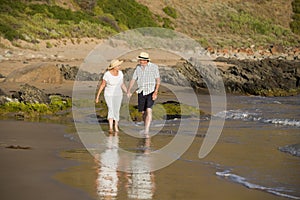 Lovely senior mature couple on their 60s or 70s retired walking happy and relaxed on beach sea shore in romantic aging together