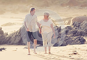 Lovely senior mature couple on their 60s or 70s retired walking happy and relaxed on beach sea shore in romantic aging together