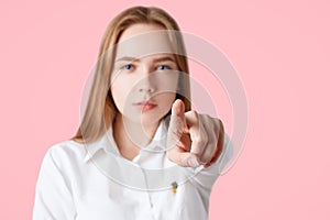 Lovely serious confident young female points at camera with fore figer, chooses someone, isolated on pink background, focus on han