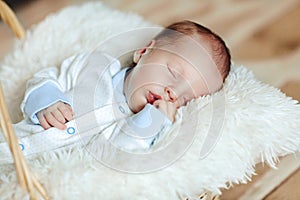 Lovely sleeping newborn boy is dressed in overalls and booties lies in the basket