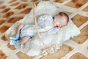 Lovely sleeping newborn boy is dressed in overalls and booties lies in the basket