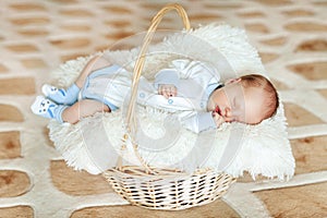 Lovely sleeping newborn boy is dressed in overalls and booties lies in the basket