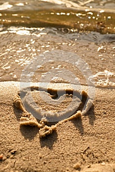 Lovely small heart sketched in salt sand at beach. Evening warm colors of sunset mirror in water level.