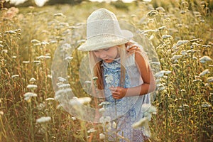 Lovely smiling blond girl in a field at sunset. Cute girl in a flowering field sniffs flowers. Ukrainian in a hat and dress near