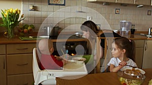 Lovely smiling housewife is cooking dinner and at the same time feeding two children in the kitchen. Woman peeks into