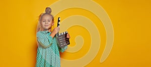 Lovely smiling little girl holding director's film movie slateboard over yellow studio background. Concept of human