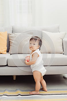 Lovely standing baby next to the sofa. Cute portrait of happy face baby girl