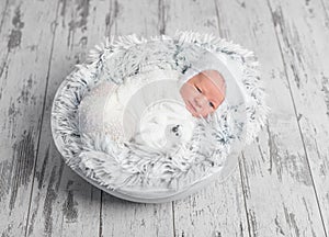 Lovely swaddled newborn lying with toy in basket