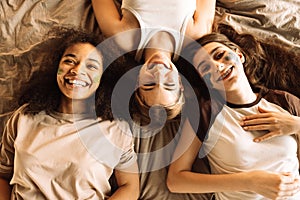 Lovely teenagers of different races apply cosmetic masks to their faces in the bedroom. Multiethnic friends are lying on the bed photo