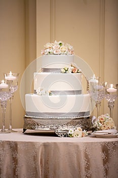 Lovely Three Tiered White Frosting with Grey Trim and Roses on a Table with Candles for a Wedding Ceremony