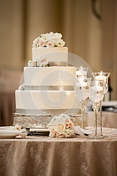 Lovely Three Tiered White Frosting with Grey Trim and Roses on a Table with Candles for a Wedding Ceremony