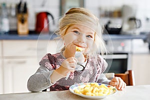 Lovely toddler girl eating healthy fried potatoes for lunch. Cute happy baby child in colorful clothes sitting in