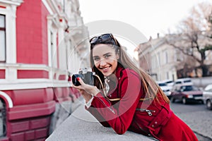 Lovely white woman in stylish red attire taking picture of street view. Elegant funny photographer smiling during