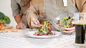 A lovely wife is serving a salad on a plate after cooking it with her husband in the kitchen